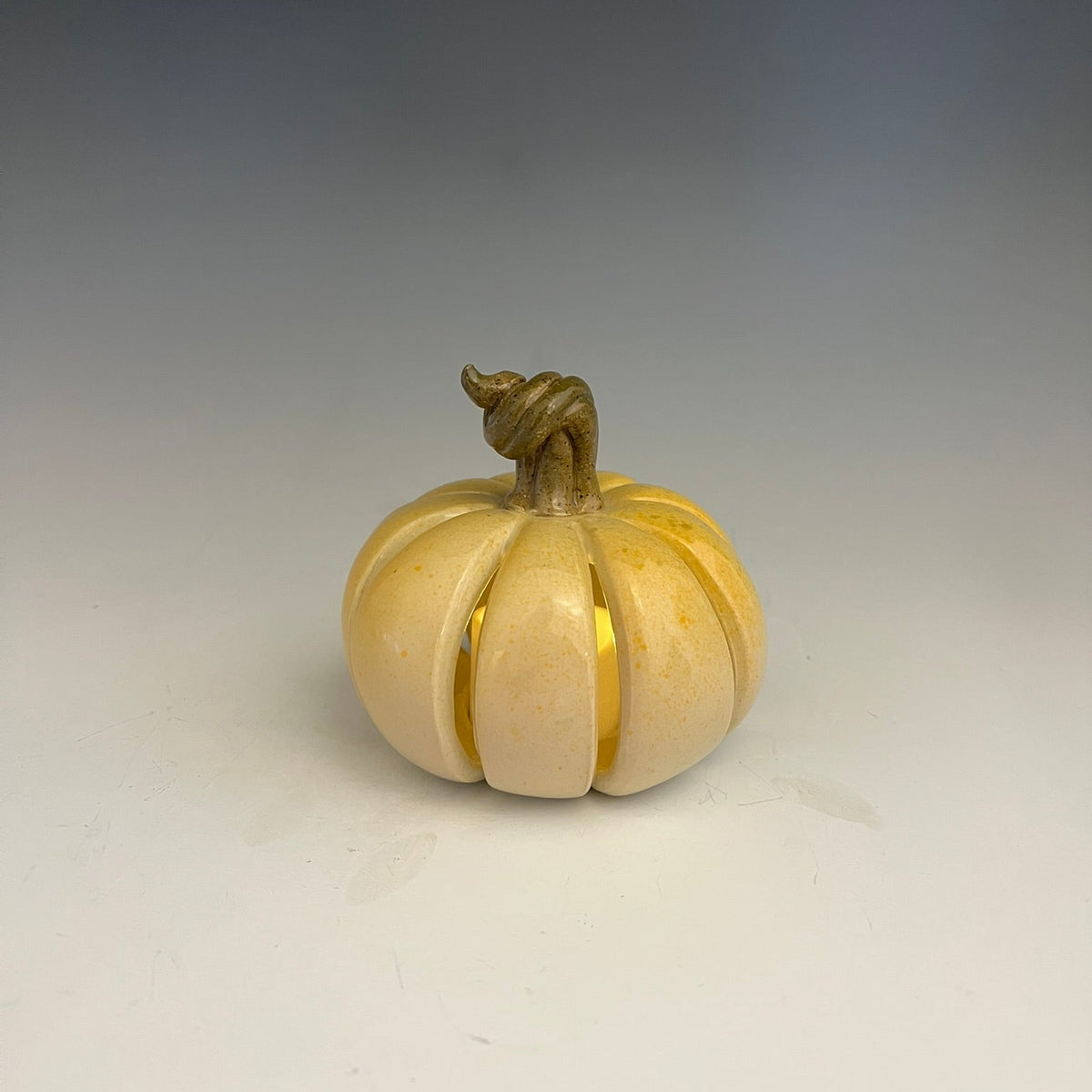 A small carved pumpkin-shaped decorative object with a twisted stem, shown on a plain light gray studio background.