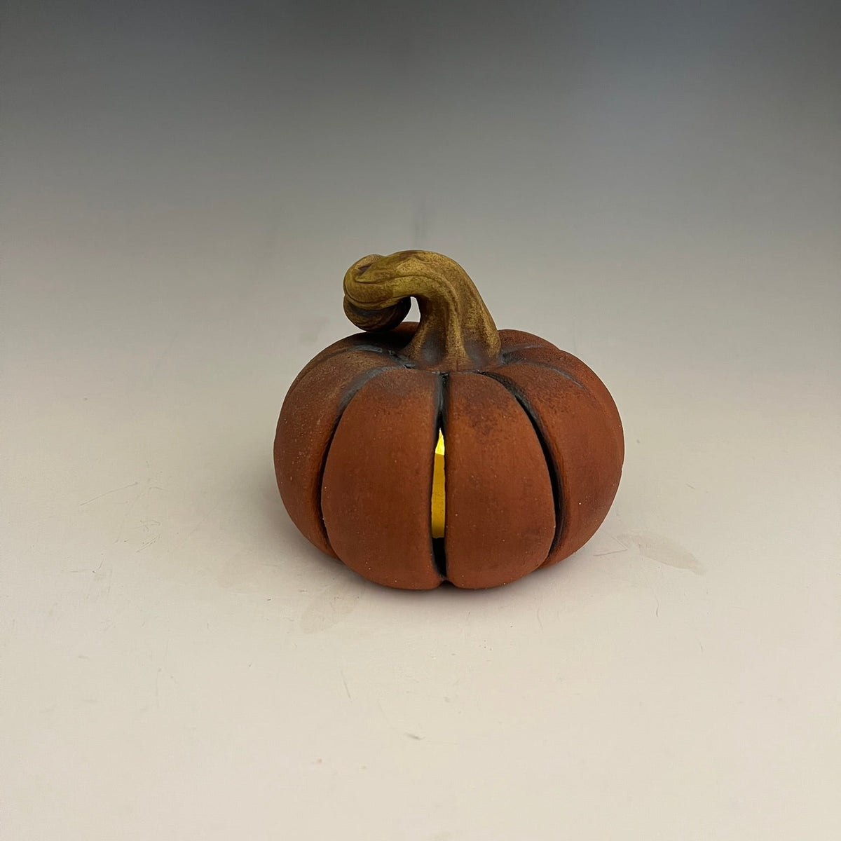 A small decorative pumpkin-shaped object with a curved handle, shown on a plain light background.